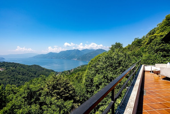 Eine Terrasse mit Blick auf einen See und Berge, mit Geländer und einem Tisch mit Stühlen.