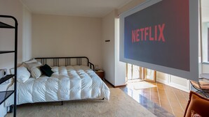 A bedroom with a bed, a TV screen displaying 'NETFLIX,' a window, and a radiator. - Groovy House: Vintage Charm, Lake Views, and Nature Retreat (Agra)
