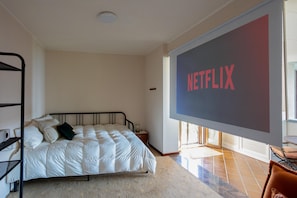 Ein Schlafzimmer mit einem Bett, einem Fernseher, der 'NETFLIX' anzeigt, einem Fenster und einer Heizung.
