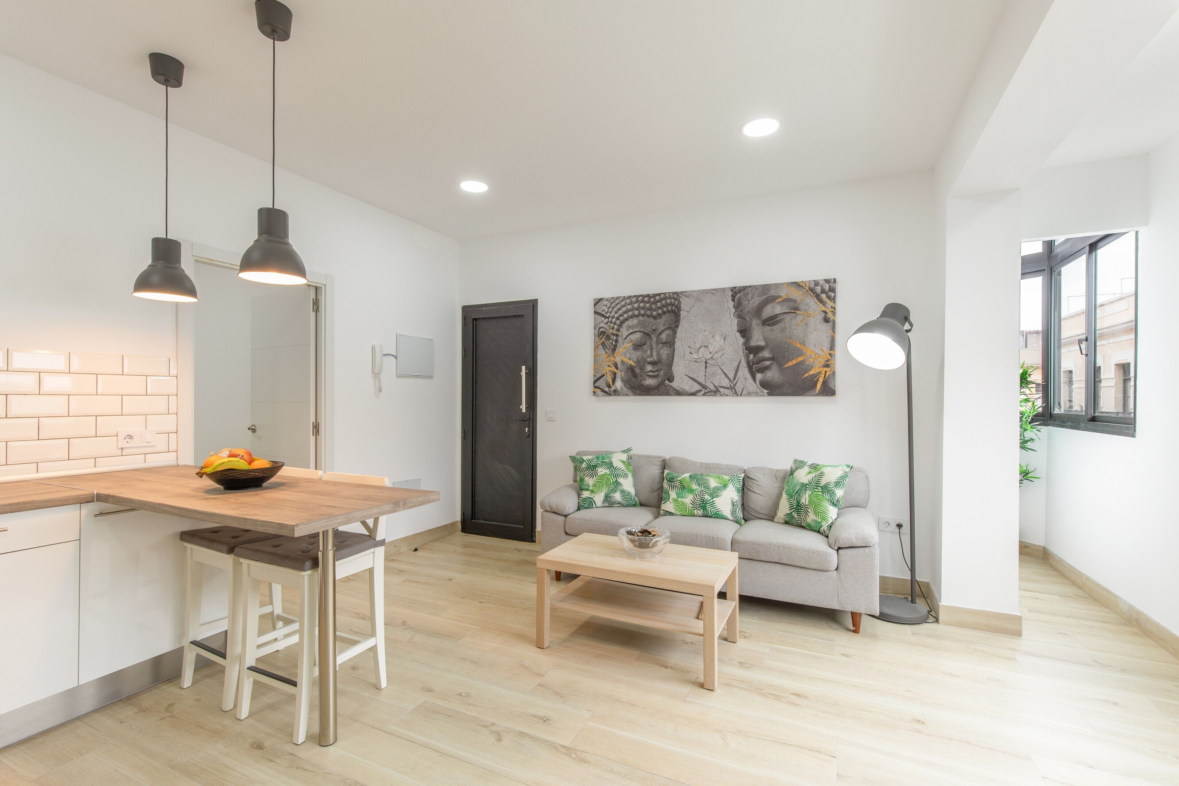 Ein modernes Wohnzimmer mit Küchenbereich, einem Esstisch, einer Couch mit Kissen, einem Couchtisch und einer Buddha-Statue an der Wand.