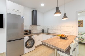 Eine moderne Küche mit einem Edelstahl-Kühlschrank, einer Waschmaschine, einem Holzespeisetisch mit Obstschale, Pendelleuchten und einer gefliesten Spritzschutzwand.