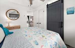 Ein Schlafzimmer mit Bett, Schminktisch, Spiegel, einer Tür und einem Wandzeichen.
