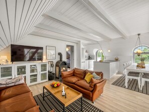 Ein geräumiger Wohnbereich mit Kamin, Fernseher und einer Küche im Hintergrund.