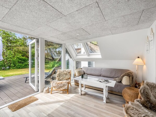 Ein modernes Wohnzimmer mit einer Couch, einem Sessel und einem Couchtisch, großen Fenstern und einer Holzterrasse.