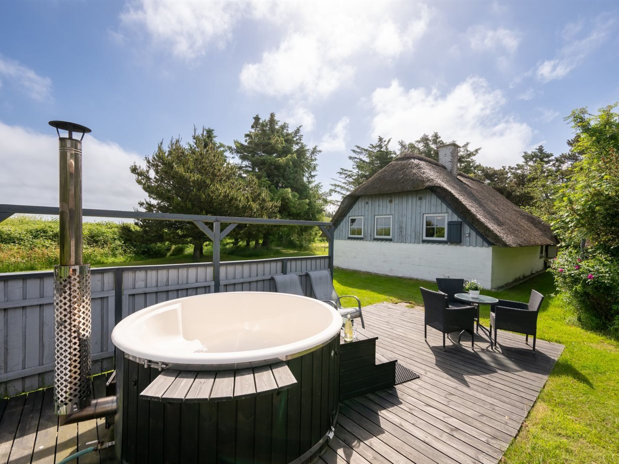 Um deck de madeira com hidromassagem, móveis de exterior e uma casa com telhado de palha.