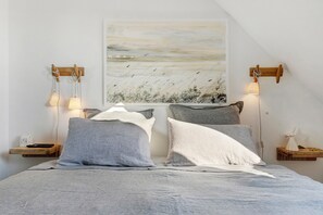 Ein Schlafzimmer mit Bett, Kissen, einem Nachttisch, einer Wandlampe und einem Bild.
