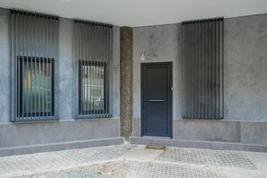 Un edificio moderno con una puerta oscura, ventanas con barrotes y una pared con textura.