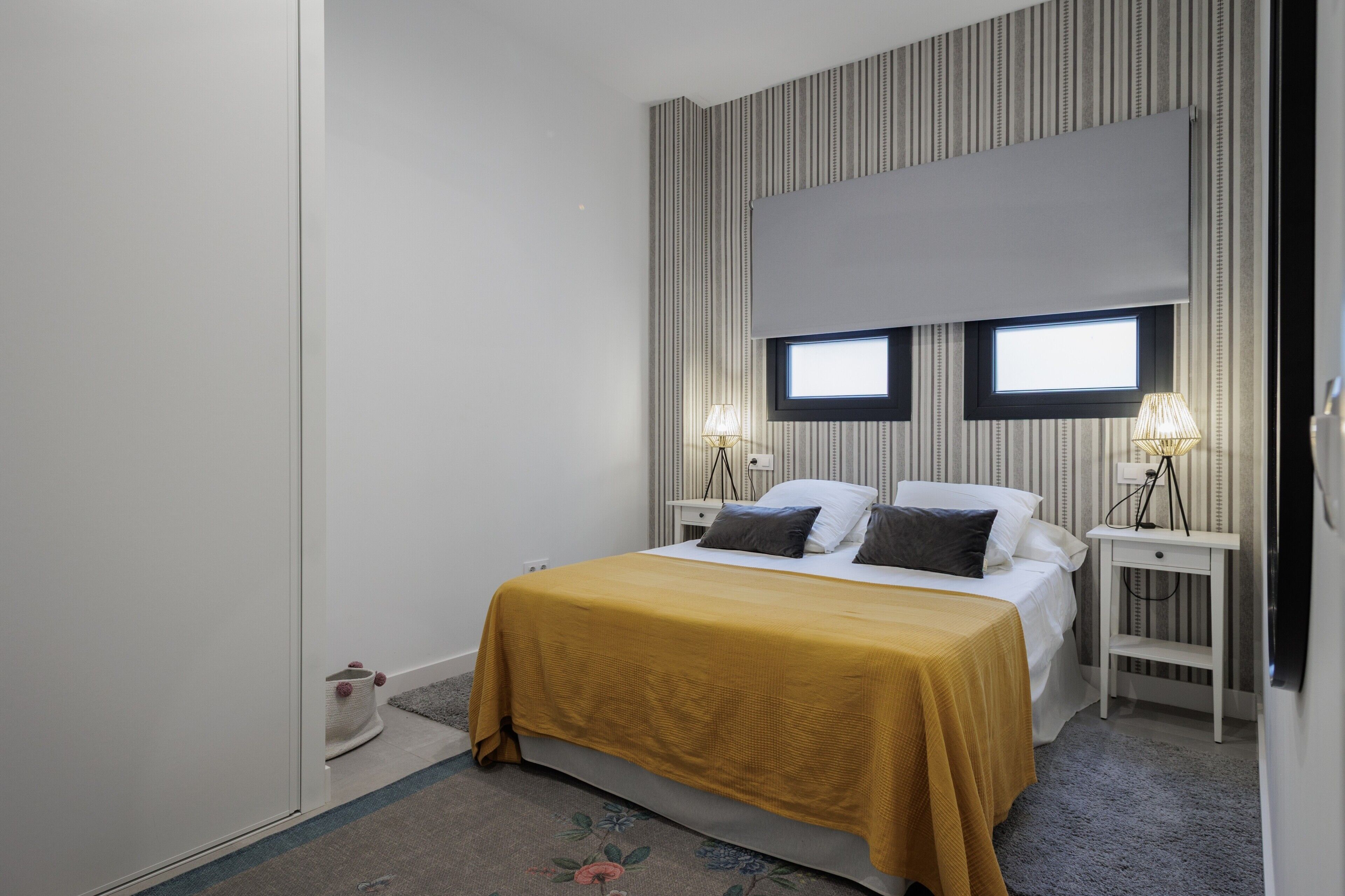 A bedroom with a bed, two bedside lamps, a window, and a curtain.