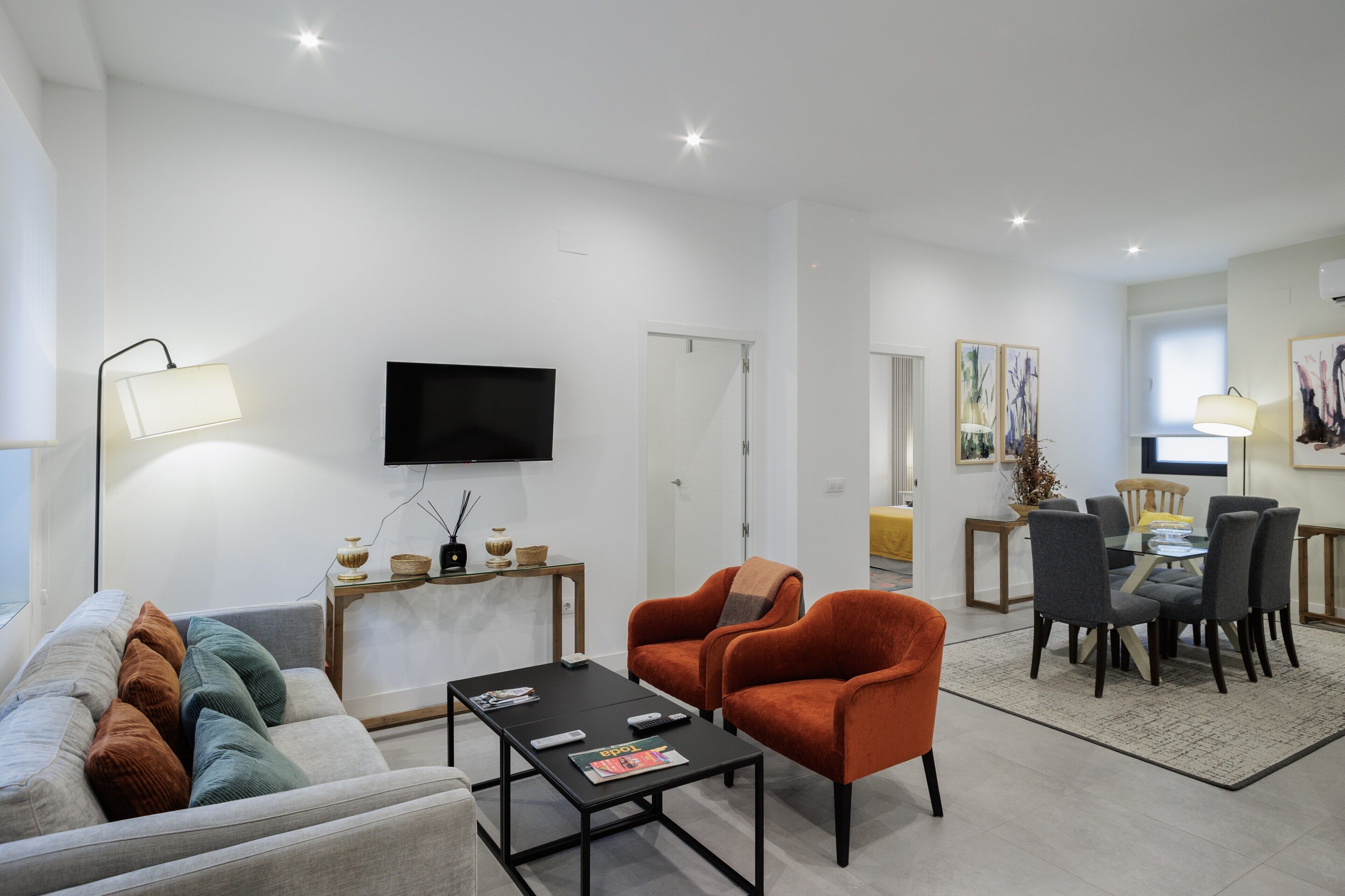 A living room with a sofa, armchairs, a coffee table, a TV, and a dining area with chairs and a table.