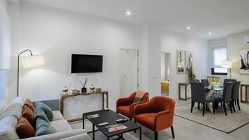 A living room with a sofa, armchairs, a coffee table, a TV, and a dining area with chairs and a table.