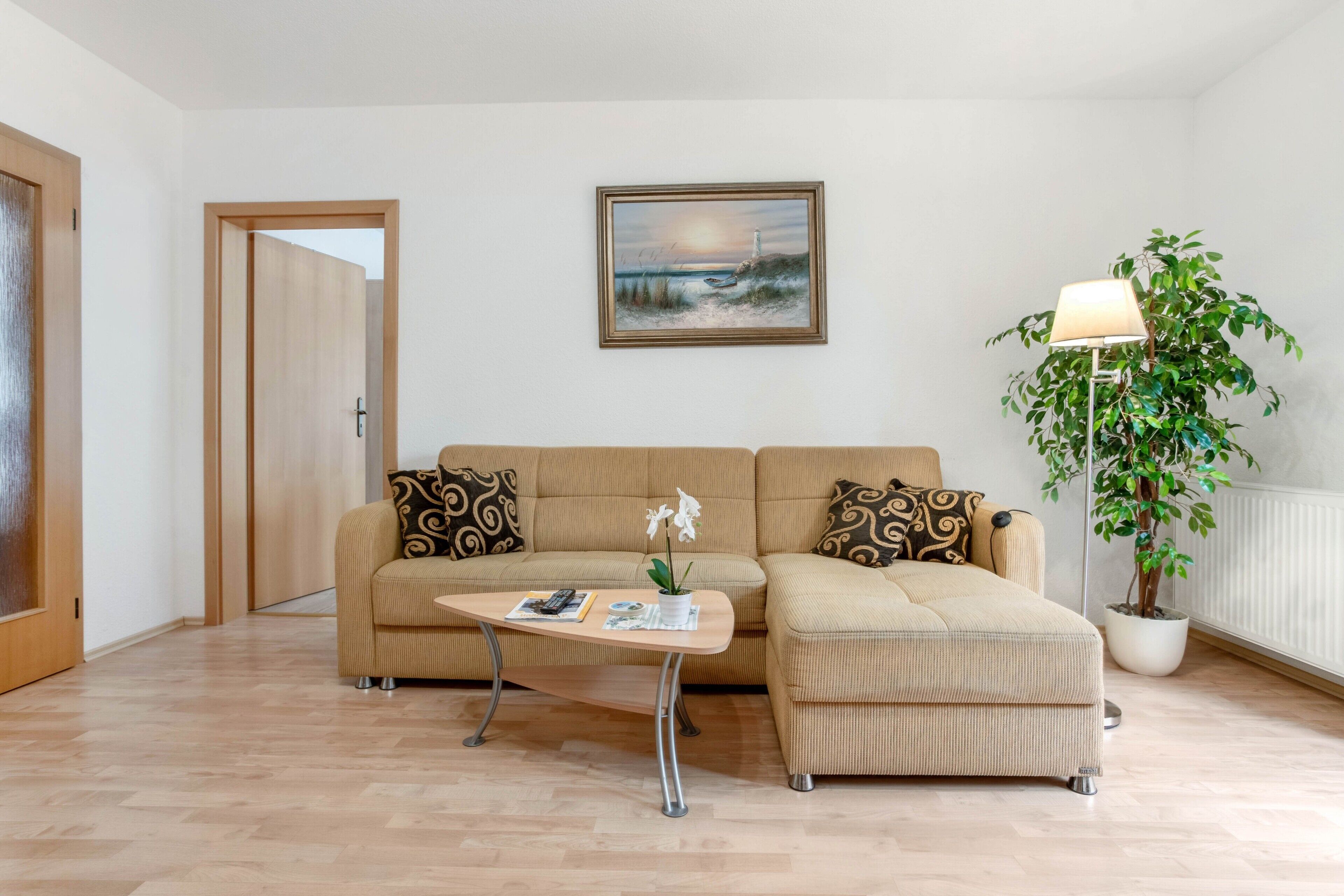 Un salon avec un canapé, une table basse, un tableau, une lampe et une plante en pot.