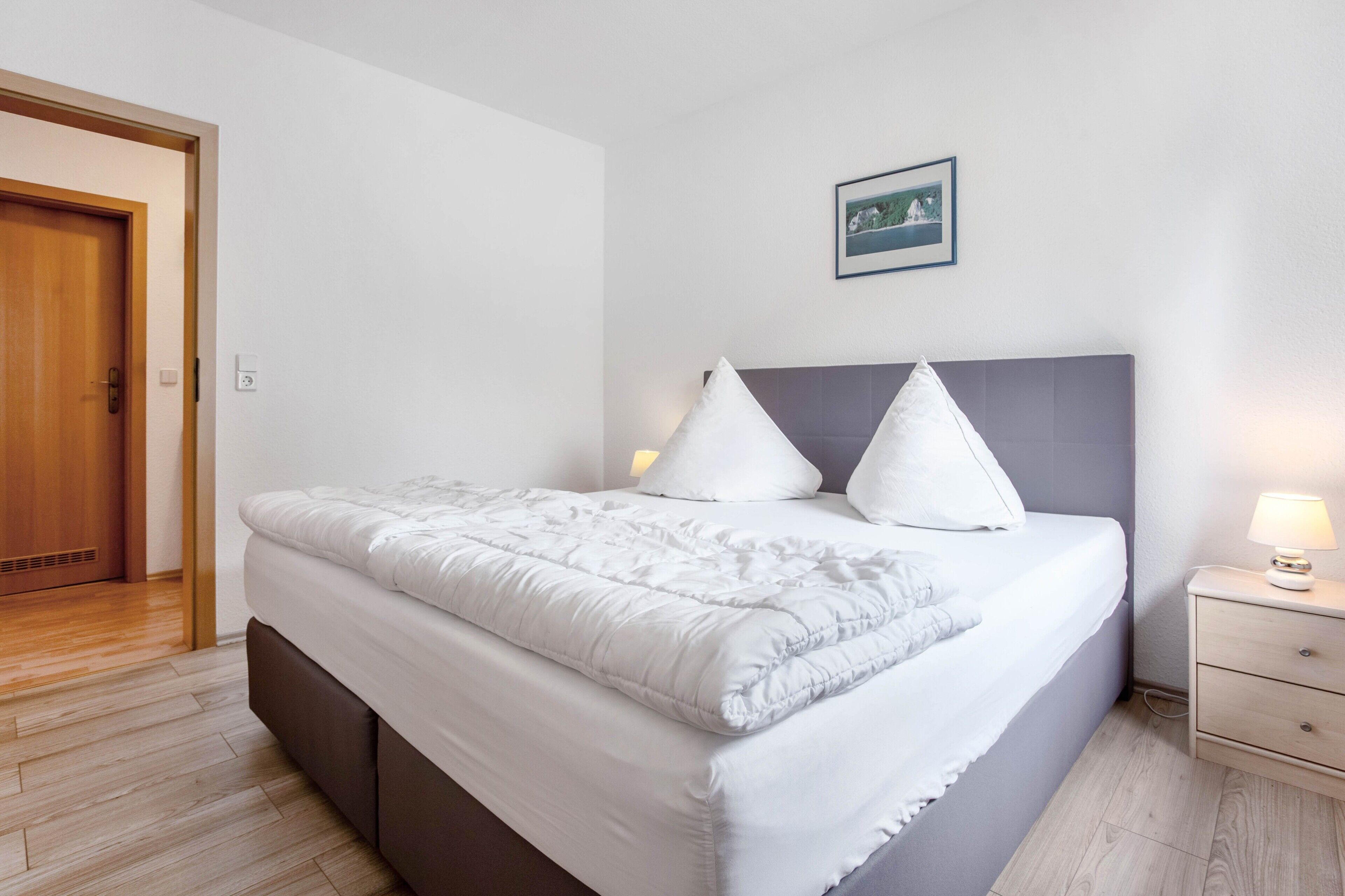 A neatly made bed with a headboard, a bedside lamp, and a framed picture on the wall.