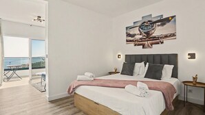 A modern hotel room with a large bed, a painting above it, and a balcony with a view. - Holiday Home 'Lobo's House' with Sea View, Private Terrace and Wi-Fi (Câmara de Lobos)