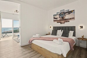 Une chambre d’hôtel moderne avec un grand lit, un tableau au-dessus et un balcon avec vue.