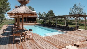 A wooden deck with a pool, lounge chairs, and a thatched-roof structure. - Mas de Dard, an Exceptional Estate in Provence, with a heated pool and a padel court (Saintes-Maries-de-la-Mer)