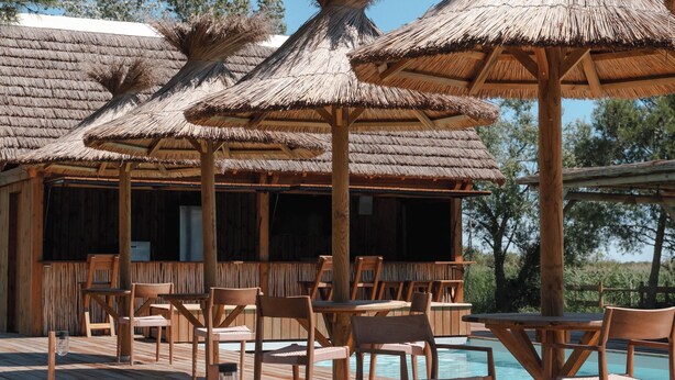 A wooden deck with thatched umbrellas and chairs, a pool, and a building with wooden walls. - Mas de Dard, an Exceptional Estate in Provence, with a heated pool and a padel court (Saintes-Maries-de-la-Mer)