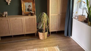Et værelse med et træskab, en makramevægophæng, et indrammet billede, en potteplante og et vindue med udsigt.