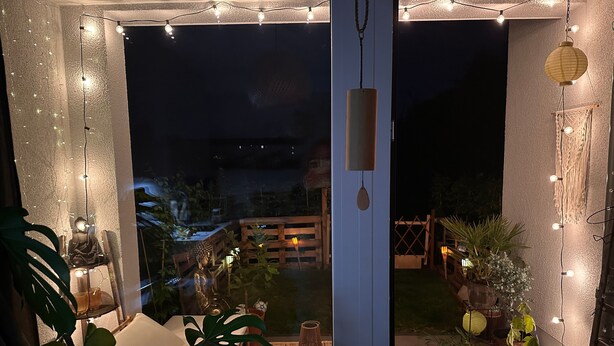 Et hyggeligt udendørs område med lyskæder, en træbænk og plantekasser.