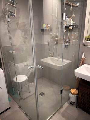 Een douchecabine met glazen wanden, een wastafel, toilet en opbergplanken.