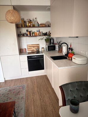 Een moderne keuken met witte kasten, een houten aanrecht, een inbouwoven, een magnetron en een spoelbak.