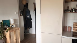Et moderne køkken med hvide skabe, en hængende vævet lampe og et træskab med en plante.