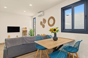 A modern living room with a sofa, a dining table with chairs, a TV, and a window with a view. - Casa El Limonero: Private Pool, Wi-Fi & Air Conditioning in Conil de la Frontera (Conil de la Frontera)