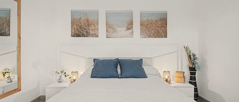 Un dormitorio con una cama grande, dos mesitas de noche, un espejo y tres cuadros en la pared.