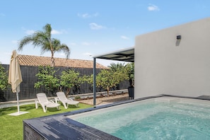 A swimming pool with a covered area, a tiled roof, and a fenced garden with palm trees and shrubs. - Casa El Limonero: Private Pool, Wi-Fi & Air Conditioning in Conil de la Frontera (Conil de la Frontera)