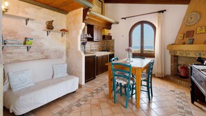 A cozy kitchen with a dining area, a sofa, and a view through a window. - Panoramic Apartment in Villa (Torre dei Corsari)