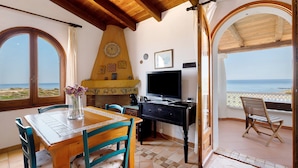 A dining area with a wooden table and chairs, a television, and a view of the sea through an open archway. - Panoramic Apartment in Villa (Torre dei Corsari)