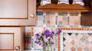 A kitchen with wooden cabinets, a tiled backsplash, and a vase with purple flowers on the counter. - Panoramic Apartment in Villa (Torre dei Corsari)