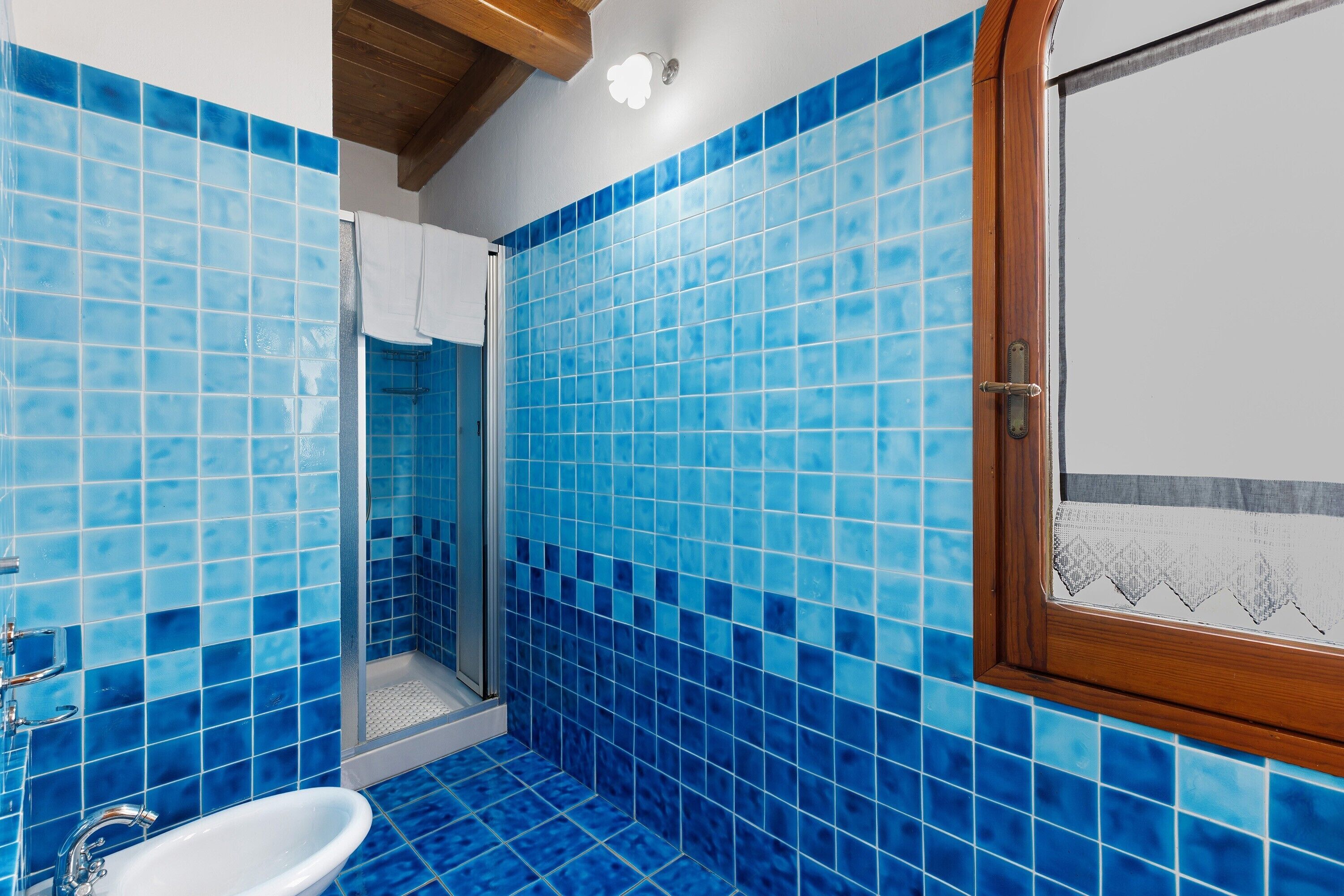 Ein Badezimmer mit blauen Fliesen, einem weißen Waschbecken und einem Fenster mit Holzrahmen.
