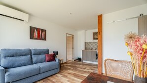 A living room with a sofa, a coffee table, a wicker chair, and a vase with dried flowers.