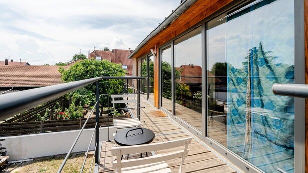 A balcony with a wooden deck, a white chair, and a table.