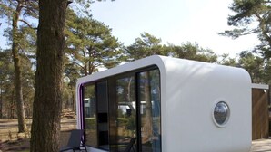 A modern, white, curved structure with large glass windows, a small circular window, and a bench outside.