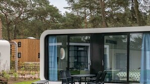 A modern mobile home with a large sliding glass door, a patio with outdoor furniture, and a garden area.