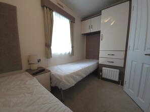 A small, clean room with two single beds, a desk with a lamp, a radiator, and a wardrobe. - Seaside Lodge- Prestatyn- Sleeps 6 (Prestatyn)