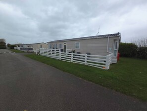 A row of mobile homes with white fences, a paved driveway, and a grassy area. - Seaside Lodge- Prestatyn- Sleeps 6 (Prestatyn)