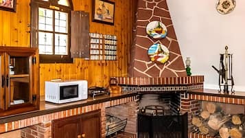A rustic kitchen with wooden walls, a stone fireplace, and a tiled floor.
