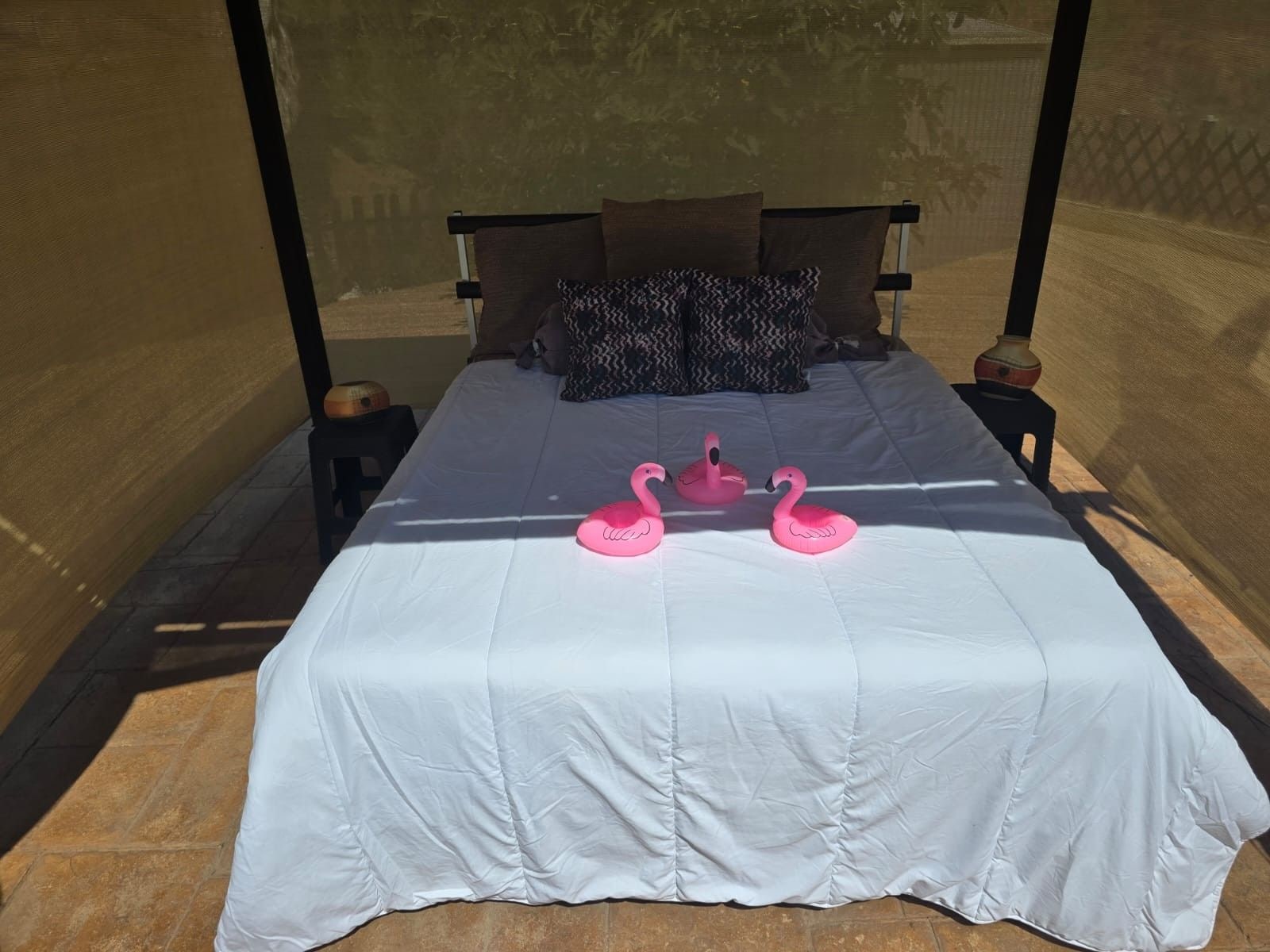 A bed with a white bedspread, two pillows, and two pink flamingo-shaped pillows.