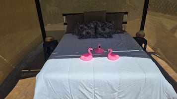 A bed with a white bedspread, two pillows, and two pink flamingo-shaped pillows.