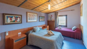 Un dormitorio con cama, mesita de noche, cómoda, ventana con cortinas y obras de arte en las paredes.