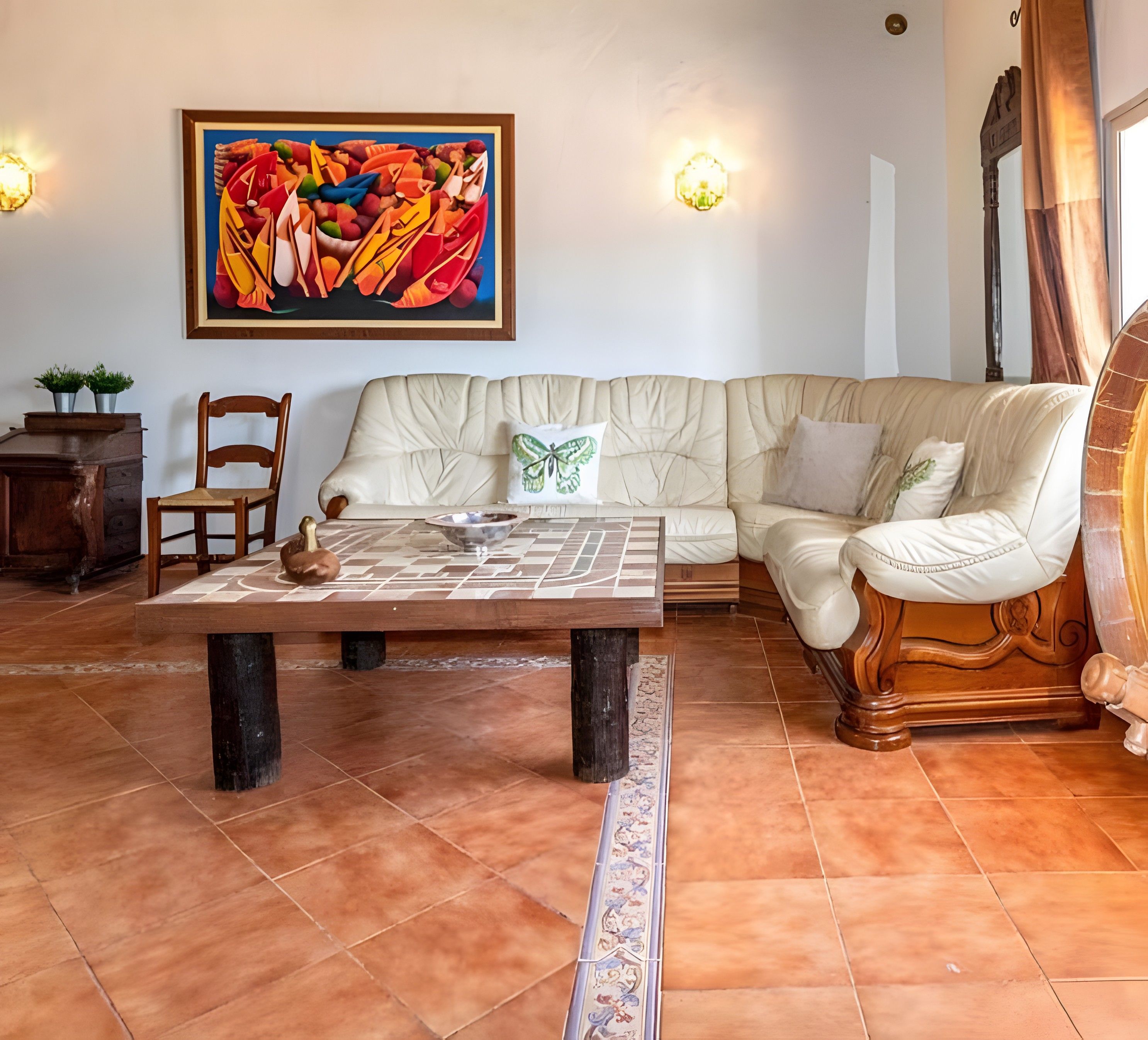 A living room with a beige sofa, a coffee table, a wooden chair, and a colorful abstract painting on the wall.