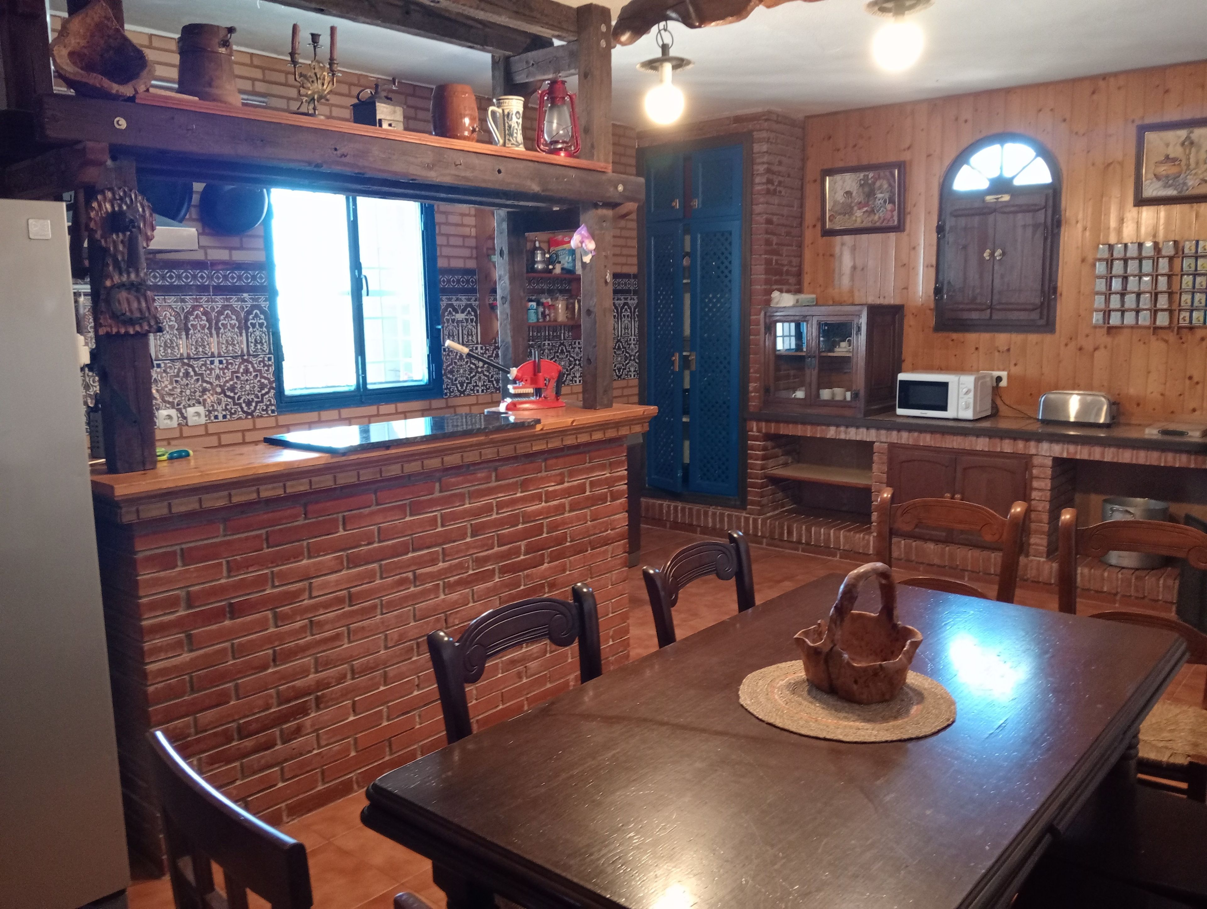 A rustic kitchen with a brick wall, wooden cabinets, and a dining area with a table and chairs.