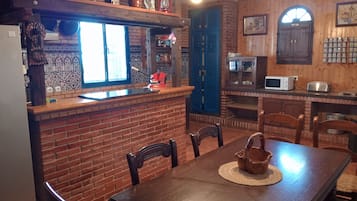 A rustic kitchen with a brick wall, wooden cabinets, and a dining area with a table and chairs.
