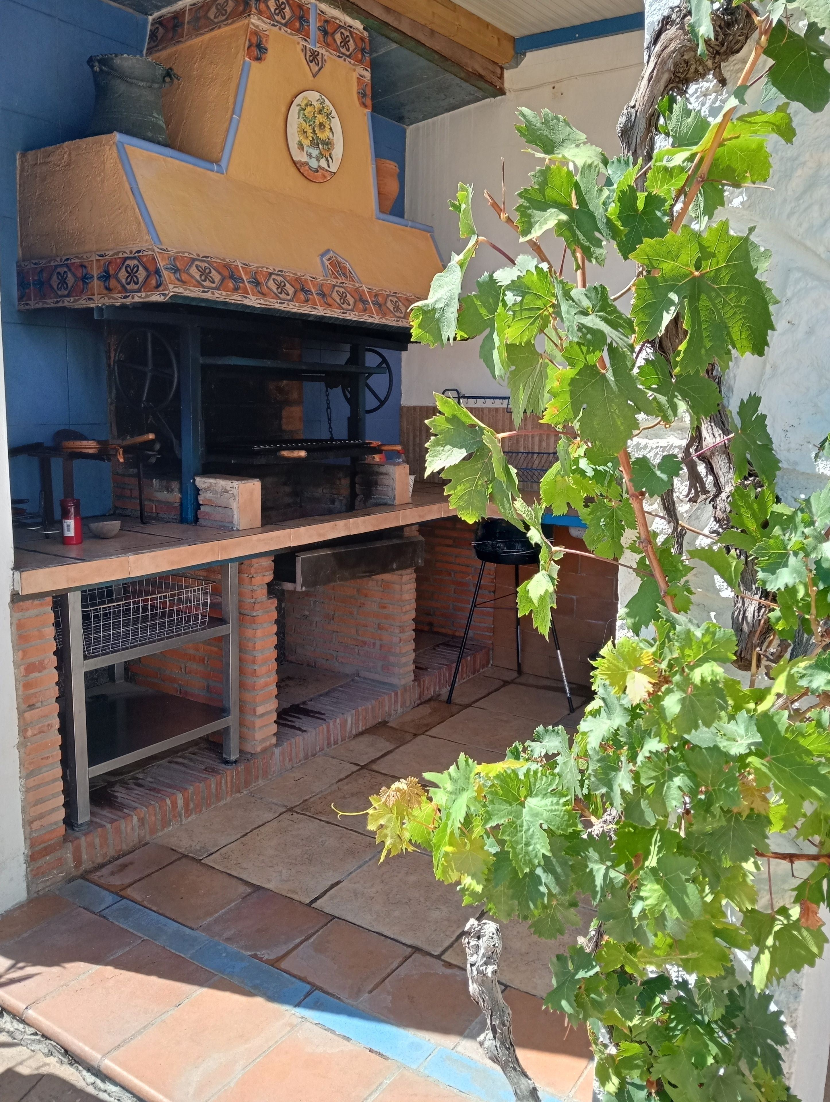 A brick-built outdoor kitchen with a chimney, a hanging pot rack, and a potted plant.