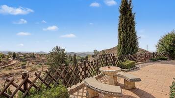 A courtyard with a stone fountain, a wooden fence, and a view of distant hills.