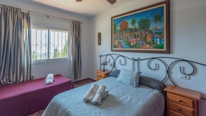 Un dormitorio con cama, mesita de noche, cortinas en la ventana y un cuadro en la pared.