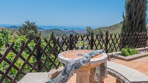 Una terraza con una mesa redonda, una hamaca y vistas al mar y a las colinas.
