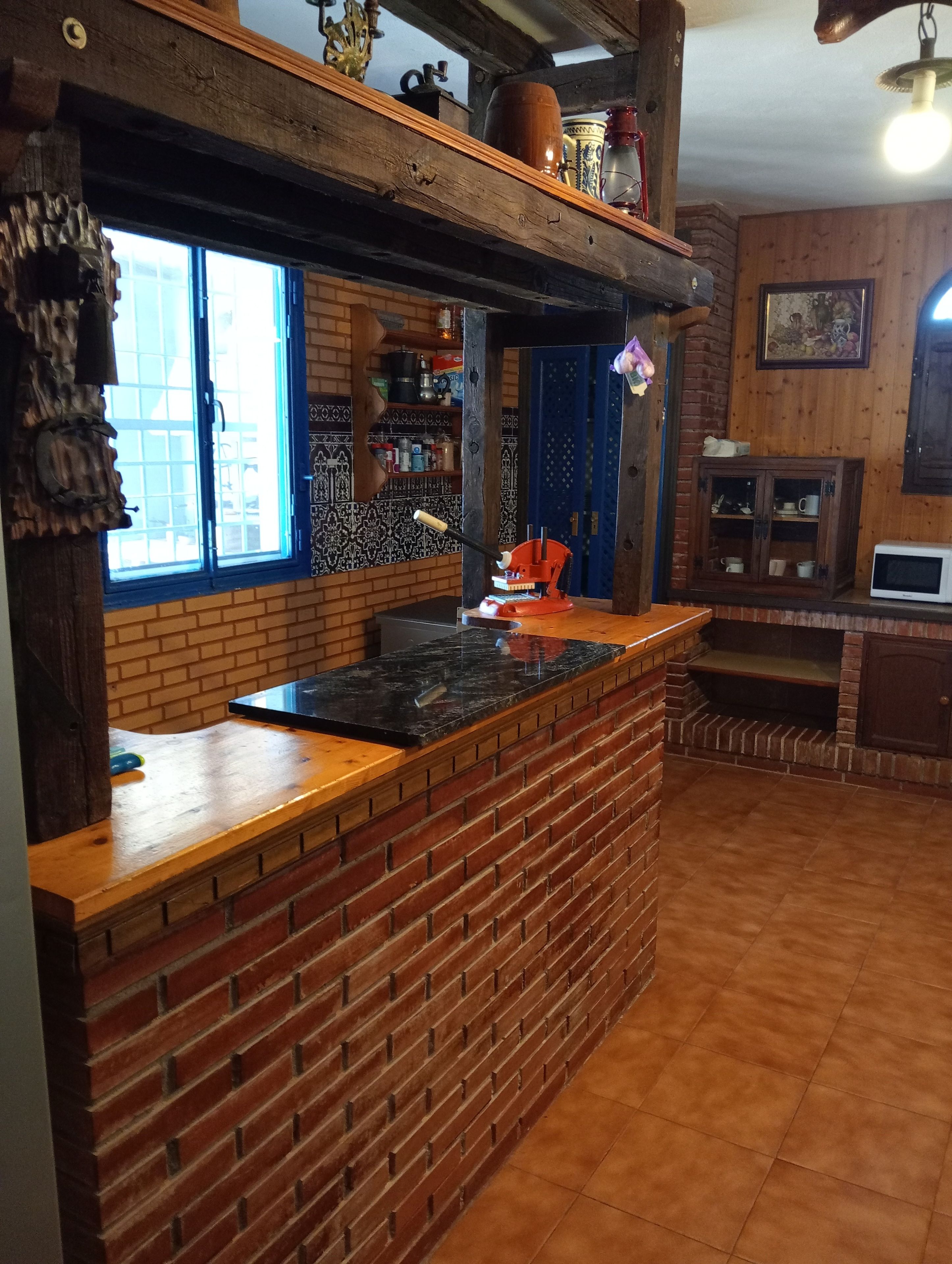 A kitchen with a brick backsplash, wooden countertop, and a window with blue shutters.